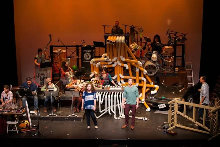 Performers on stage with a bunch of scrap metal in "The Music of Junk" musical.