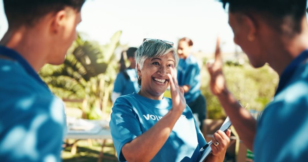 A woman wearing a 'volunteer' shirt waves at 2 other people